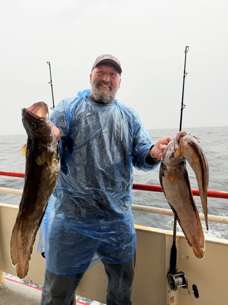 Person in rain poncho holding two large fish on a boat.