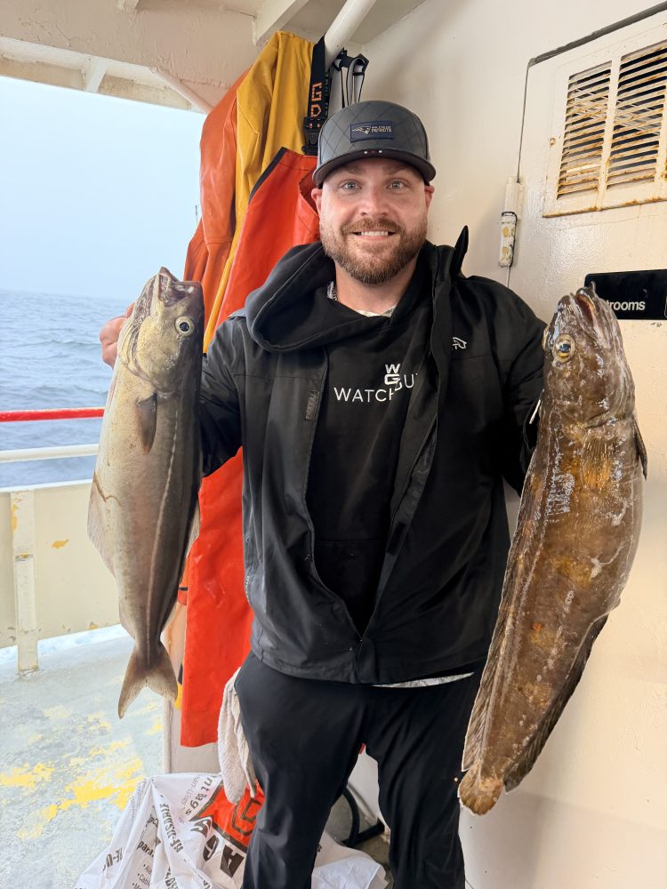 Man holding two large fish on a boat with ocean in the background.