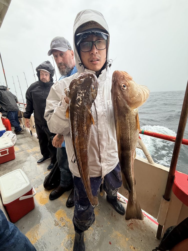Person holding two large fish on a boat with others in the background.