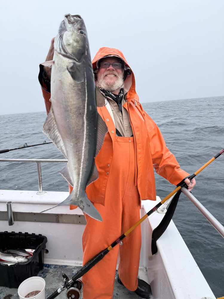 Person in orange rain gear holding a large fish on a boat.