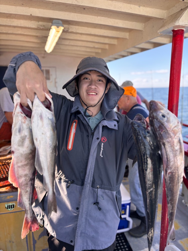 Person holding multiple fish on a boat deck, wearing a rain jacket and hat.