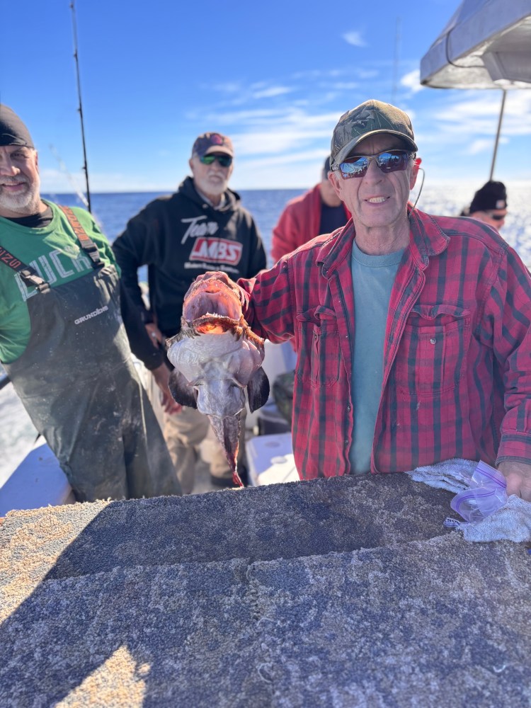 Group of men on a boat, one holding a large fish with an open mouth.