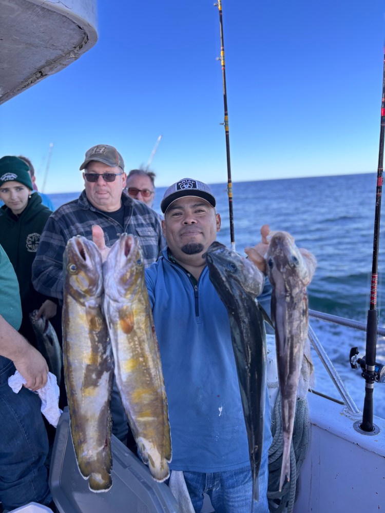 Man proudly holding two large fish on a boat with others in the background.