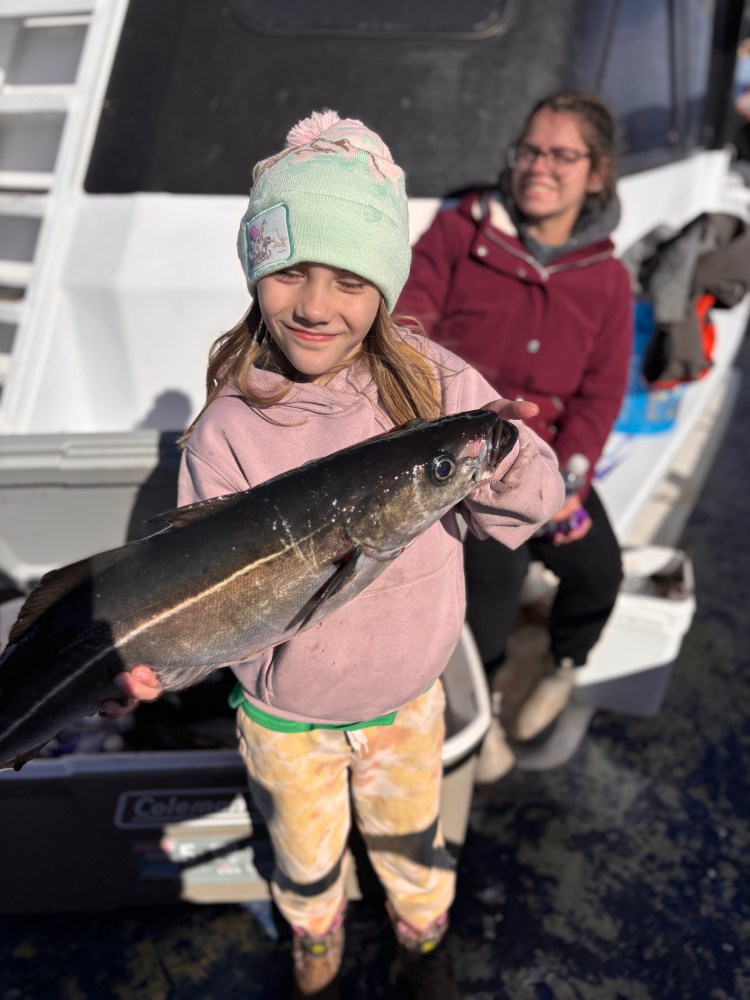 Child holding a large fish on a boat, with a woman smiling in the background.
